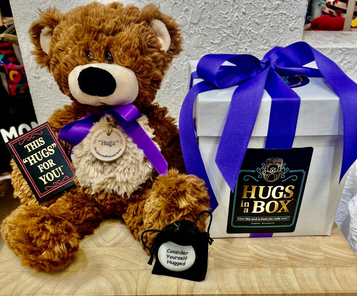 Medium-sized teddy bear with a soft brown coat, purple ribbon, and wooden “Hugs” tag, paired with a decorative Hugs in a Box gift package.